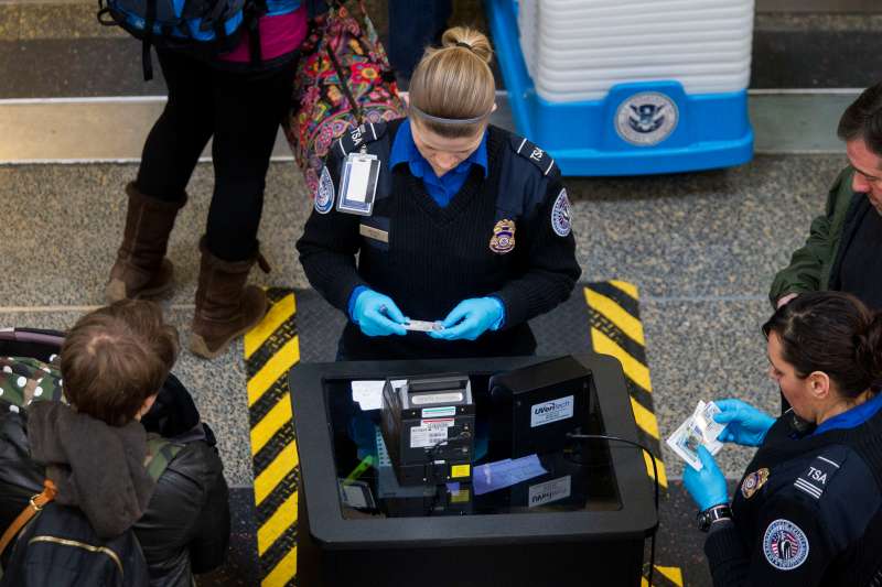 Transportation Security Administration (TSA) officers check passenger's identification at a security checkpoint at Ronald Reagan National Airport (DCA) in Washington, D.C., U.S., on Wednesday, Feb. 25, 2015. Financing for the U.S. Department of Homeland Security (DHS) is set to lapse after Friday and the agency would face a partial shutdown unless Congress provides new money. More than 200,000 government employees deemed essential at DHS, including TSA officers, would still have to report to their posts, even though their pay would stop unless Congress finds a solution. Photographer: Andrew Harrer/Bloomberg via Getty Images