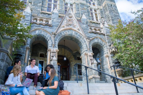 group of students sit on the steps of the main building entrance at Georgetown University