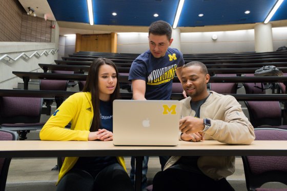 Three students looking at a laptop in a classroom at The University of Michigan Ann Arbor